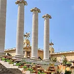 Patru coloane mari de piatră într-un peisaj urban cu arhitectură clasică și vegetație decorativă
