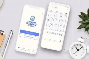 Două telefoane mobile afișează o aplicație de puzzle Sudoku, alături de un ceas alb și o plantă verde pe un birou