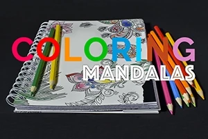 Creioane colorate așezate pe un carnet de colorat cu mandale pe un fundal negru
