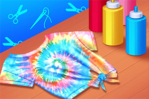 Tricou tie-dye colorat, așezat pe o masă din lemn, cu trei sticle de vopsea roșie, galbenă și albastră pe fundal albastru cu simboluri de croitorie