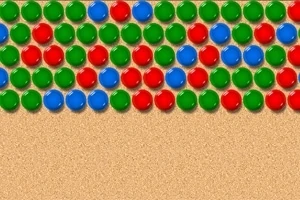 Bile de culori roșu, verde și albastru așezate în linii pe un fundal nisipos