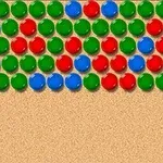 Bile de culori roșu, verde și albastru așezate în linii pe un fundal nisipos