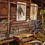 Cabana din lemn cu verandă, având diverse obiecte suspendate, cum ar fi geantă, roți și haine, pe un fundal de vegetație tropicală
