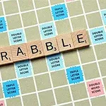 Piese din lemn cu literele formând cuvântul SCRABBLE pe o tablă de joc cu pătrate colorate pentru punctaj