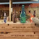 O mână ține un pistol și trage spre sticle plasate pe cutii de lemn, iar o sticlă verde se sparge