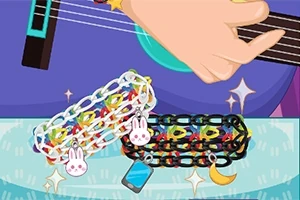 O mână cântă la o chitară albastră, iar pe masă sunt două brățări colorate cu charmuri de iepuraș, telefon și semilună
