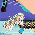 O mână cântă la o chitară albastră, iar pe masă sunt două brățări colorate cu charmuri de iepuraș, telefon și semilună