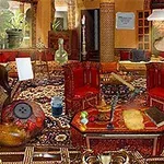 Cameră bogat decorată cu mobilier roșu și covoare orientale, plină de obiecte diverse și plante