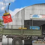 Un camion de marfă verde în fața unui depozit cu macara și container roșu suspendat