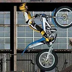 Motociclist cu echipament galben-negru executând o cascadorie pe o motocicletă de teren într-un mediu industrial