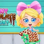 Personaj animat cu păr blond și fundă roz ținând o tavă de ciocolată decorată, lângă un text colorat care spune „Yummy Chocolate Factory”