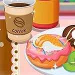 Cafea într-un pahar de hârtie lângă un platou cu două gogoși decorate cu frișcă, fructe și glazură, alături de felii de kiwi